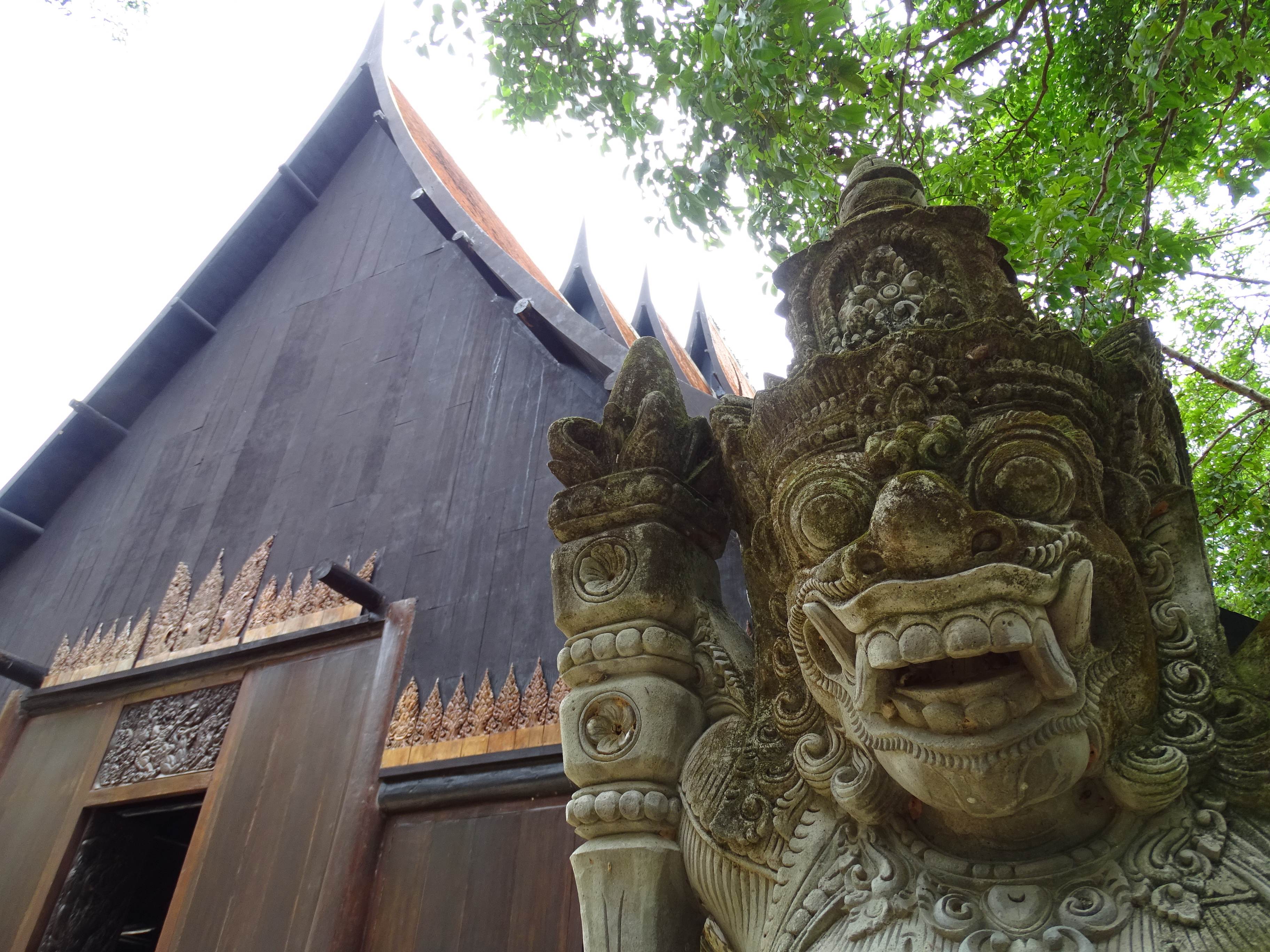 A dark wooden hall at Baan Dam, the Black House, with a carved stone guardian in front